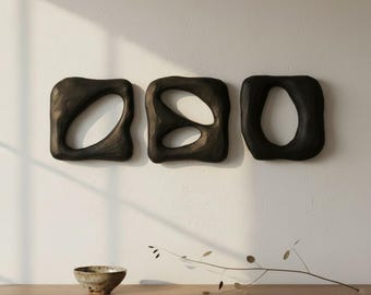 May include: Three black, irregularly shaped, hollow wall sculptures with smooth, rounded edges. Each piece features a unique, organic cutout design. The sculptures are mounted horizontally in a row, displaying a matte finish and a solid, dark appearance.