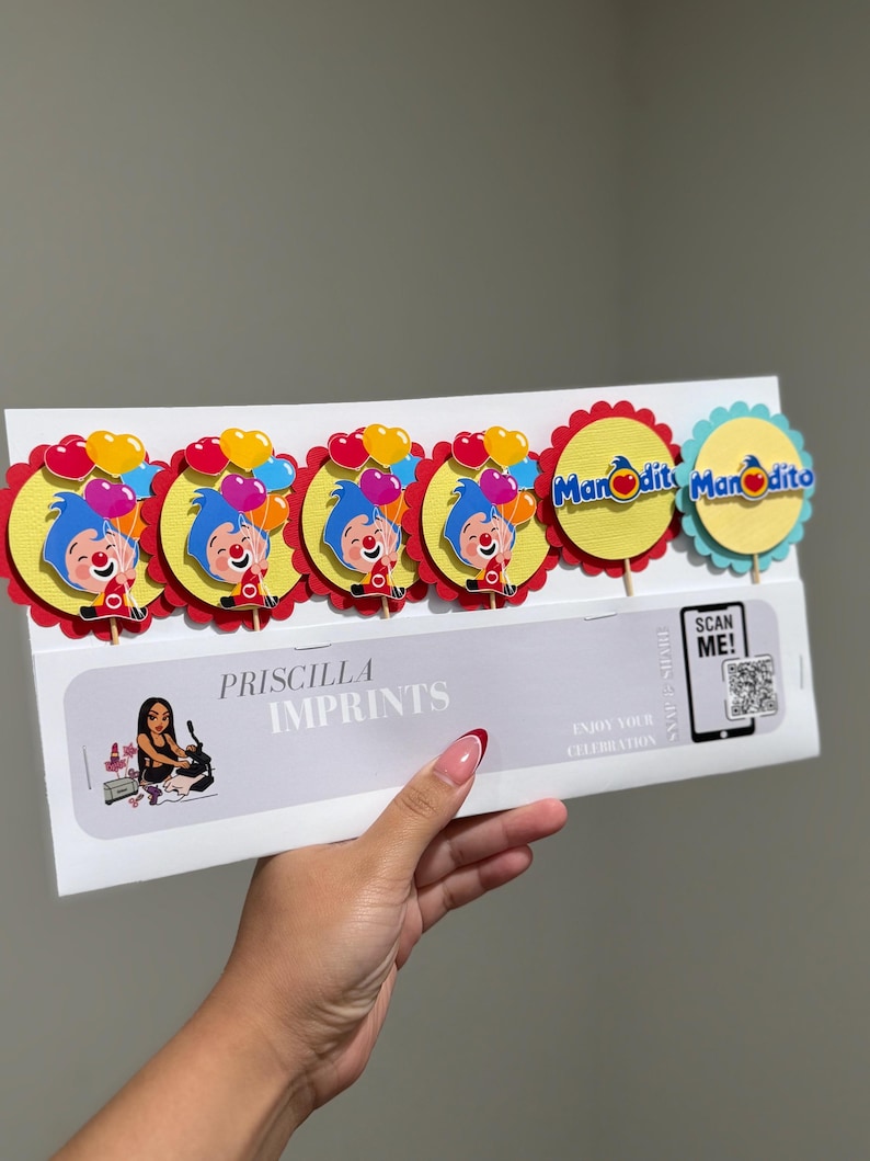 May include: A package of cupcake toppers featuring a cartoon clown with blue hair and a red nose, holding colorful balloons. The toppers are on yellow and red scalloped circles. The package includes the text "Priscilla Imprints".