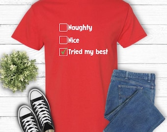 May include: A red t-shirt with the text "Naughty, Nice, Tried my best" in white. The shirt is paired with blue jeans and black and white sneakers. A small green plant is also in the image.