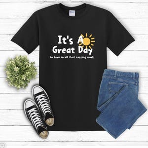 May include: Black t-shirt with white text that reads "It's A Great Day to turn in all that missing work". A yellow sun with rays is above the word "A".