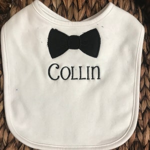 May include: White baby bib with a black bow tie and the name "COLLIN" embroidered in black.
