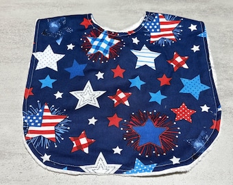 Puede incluir: Babero para bebé azul marino con estrellas rojas, blancas y azules. El diseño incluye estrellas con el patrón de la bandera estadounidense. El babero está bordeado con tela blanca.
