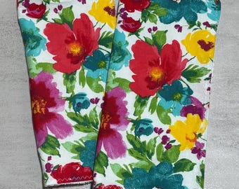 Puede incluir: Dos fundas de tela rectangulares con fondo blanco y un vibrante estampado floral en tonos rojo, magenta, verde azulado y amarillo. Los bordes están rematados con una costura decorativa en zigzag y la tela tiene un aspecto suave y texturizado.