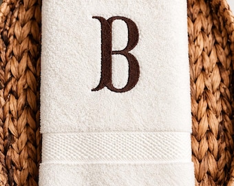 May include: A white cotton hand towel featuring a dark brown embroidered letter B in a serif font. The towel has a textured border near the bottom edge and is folded neatly. A circular green badge with the text PERSONALIZED JUST FOR YOU is visible.