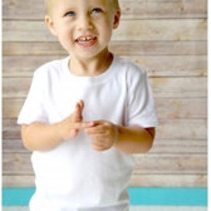 May include: A young boy wearing a white short-sleeved t-shirt and blue jeans. He has a spiky blond hairstyle and is smiling.