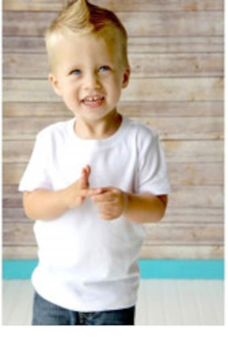 May include: A young boy wearing a white short-sleeved t-shirt and blue jeans. He has a spiky blond hairstyle and is smiling.
