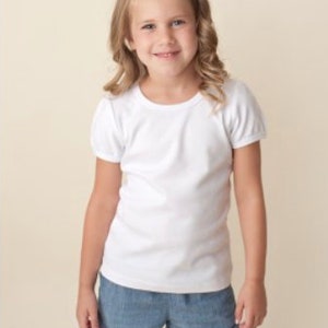 May include: A young girl wearing a white short-sleeved t-shirt and blue denim shorts.