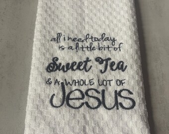 May include: A white waffle-weave kitchen towel featuring dark gray embroidered text that reads: all i need today is a little bit of Sweet Tea & A WHOLE LOT OF JESUS. The towel has a textured, grid-like pattern and a hemmed bottom edge.