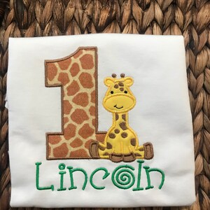 May include: White onesie with a brown and orange giraffe number one and the name "Lincoln" embroidered in green.