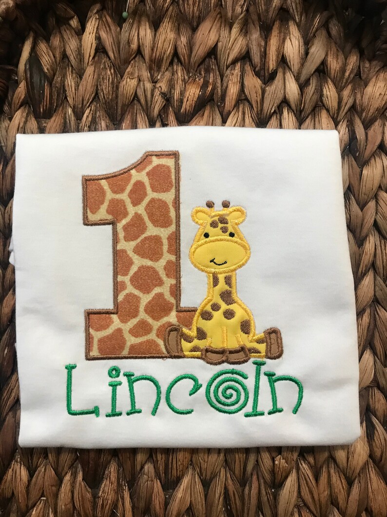 May include: White onesie with a brown and orange giraffe number one and the name "Lincoln" embroidered in green.
