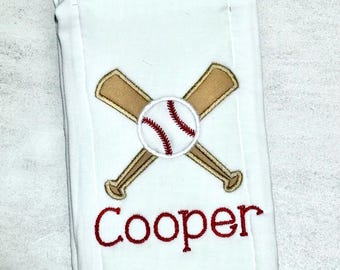 May include: A white rectangular hand towel featuring an embroidered design of two crossed tan baseball bats with a white baseball in the center. The baseball has red stitching. Below the graphic, the name Cooper is embroidered in red script.