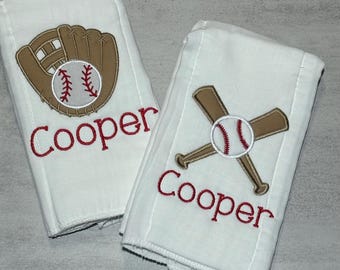 May include: Two white rectangular towels featuring embroidered baseball designs. One towel displays a brown baseball glove with a baseball, and the other shows two crossed brown baseball bats with a baseball. Both towels feature the name Cooper in red.