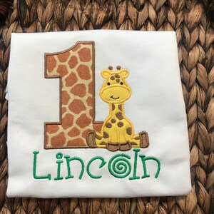 May include: White onesie with a brown and yellow giraffe-shaped number one and the name "Lincoln" embroidered in green.