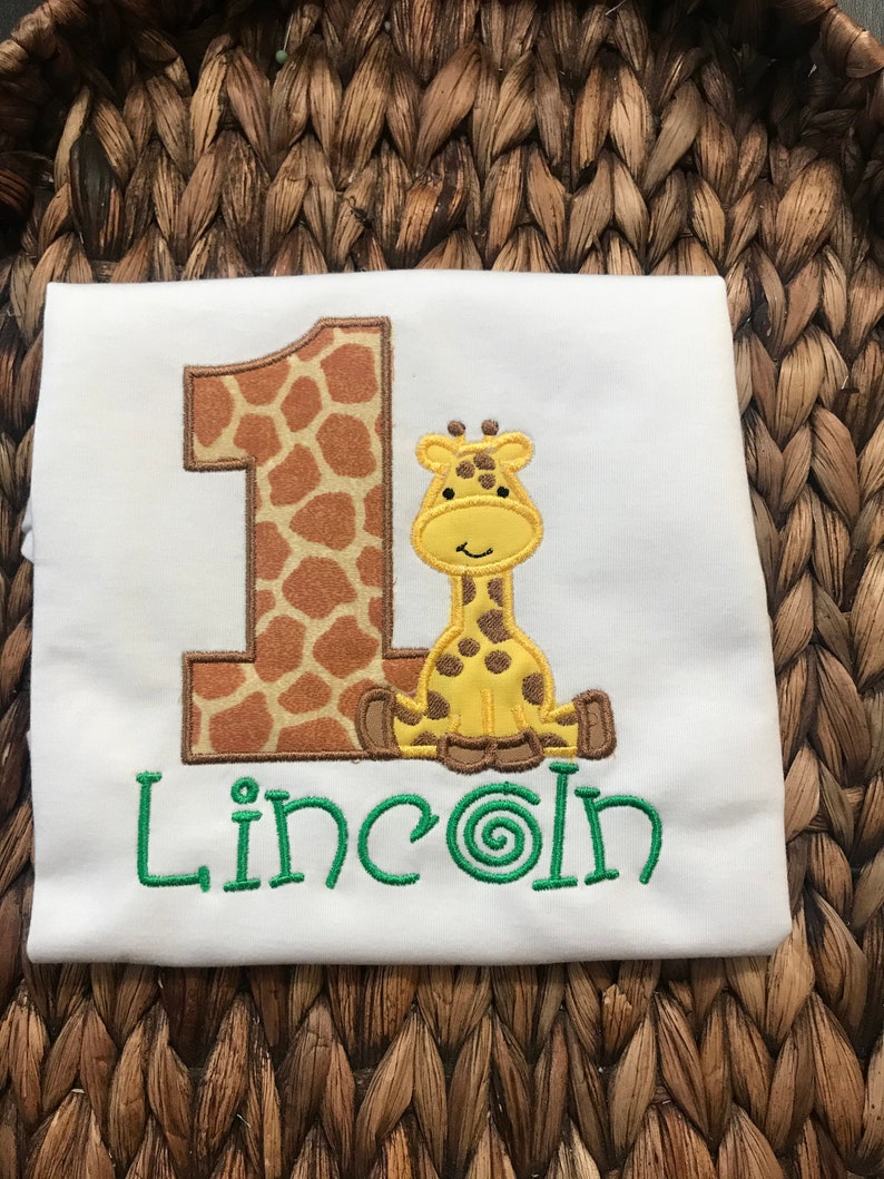 May include: White onesie with a brown and yellow giraffe-shaped number one and the name "Lincoln" embroidered in green.