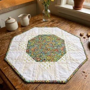 Può includere: Un sottopentola trapuntato ottagonale con un motivo floreale centrale in verde, blu e giallo. Il bordo è bianco con un motivo a pois e i bordi sono rifiniti con una stampa floreale colorata. Il sottopentola poggia su un tavolo di legno.