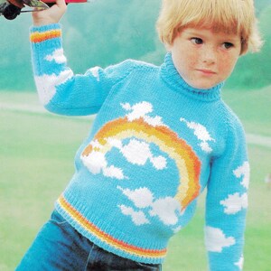 May include: A child's blue knitted sweater with a rainbow and cloud design. The sweater has a turtleneck and is paired with blue jeans. The image also includes the text "Child's Play" and "Beehive".