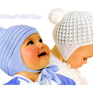 Puede incluir: Dos gorros de bebé de punto. Uno es azul claro con pompón y lazos, el otro es blanco con pompón y un patrón calado. Los gorros están diseñados para bebés.
