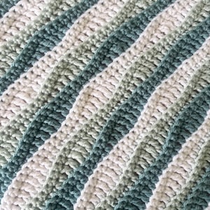 May include: A close-up of a crocheted blanket with diagonal stripes. The stripes alternate between white, light green, and a darker teal green. The texture of the crochet stitches is visible, creating a soft, textured appearance.