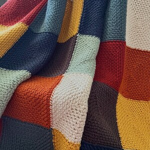 Peut inclure: Une couverture en crochet avec un motif patchwork dans des tons de brun, orange, jaune, vert et bleu.