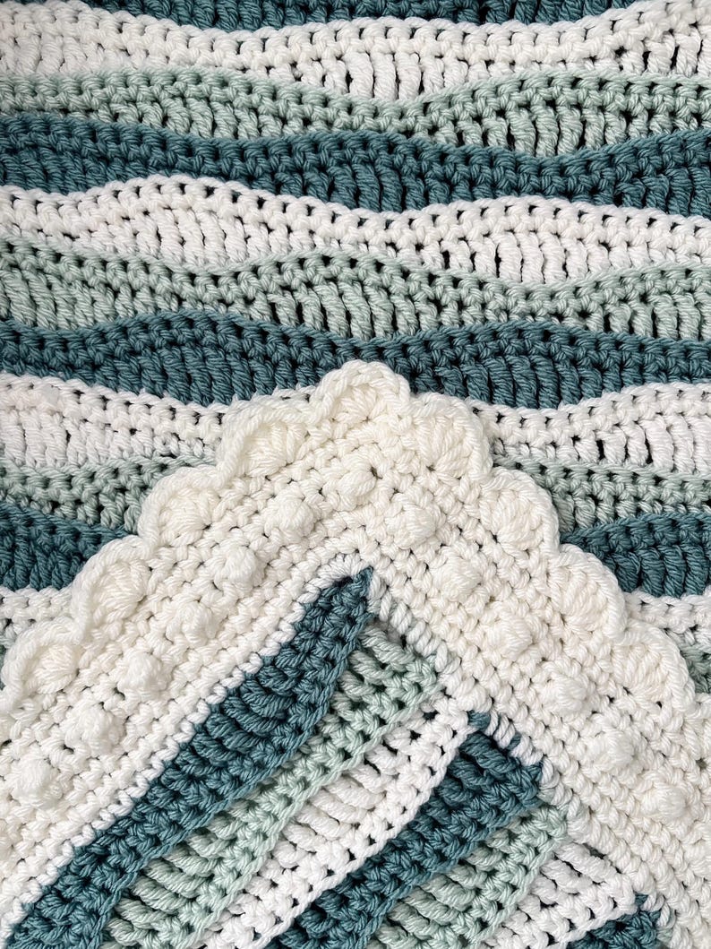 May include: A handmade crochet blanket in shades of white, teal, and light green. The blanket features a wavy pattern and a decorative scalloped edge. The yarn appears soft and the stitches are tightly woven.