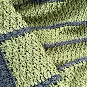 May include: Close-up of a hand-crocheted textile in shades of green and gray. The fabric features a textured stitch pattern with horizontal gray stripes. The yarn appears to be a soft cotton or similar fiber, suitable for a blanket or scarf.