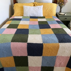 May include: A patchwork quilt with squares of pink, blue, green, yellow, and white. The quilt is made of a soft, textured fabric and is laid out on a bed with a wooden headboard.