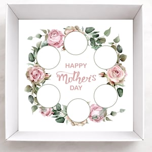 Puede incluir: Una caja blanca con un diseño floral para el Día de la Madre. El diseño presenta una corona de rosas rosas y hojas verdes que rodean seis espacios circulares. Las palabras "Happy Mother's Day" están escritas en cursiva.