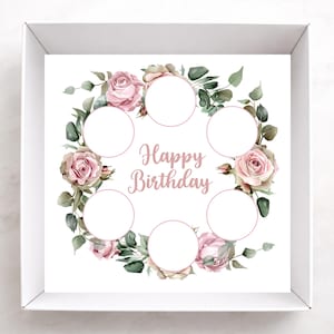May include: A white box with a floral design featuring pink roses and green leaves. The words "Happy Birthday" are written in a cursive font. The design includes six circular spaces for personalization.
