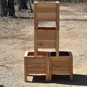 Può includere: Tre fioriere in legno impilate l'una sull'altra. Le fioriere sono in legno di cedro naturale e hanno un aspetto rustico. Ogni fioriera ha quattro gambe.