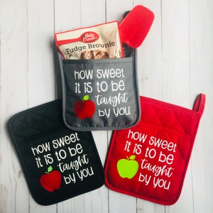 Pode incluir: Três luvas de forno cinzas e vermelhas com um bolso lateral. As luvas têm o texto "how sweet it is to be taught by you" e um gráfico de maçã.