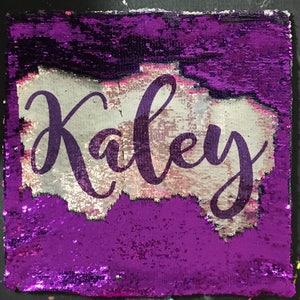 May include: Purple sequin pillow with the name "Kaley" written in white on a silver background.
