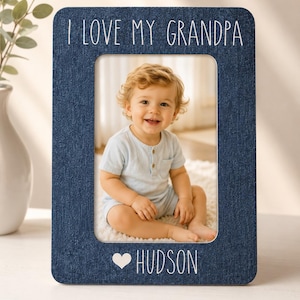 May include: A rectangular dark blue denim-textured picture frame featuring the white text I LOVE MY GRANDPA at the top and a heart symbol followed by the name HUDSON at the bottom. The frame displays a photograph of a smiling toddler.