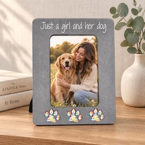 May include: A rectangular gray picture frame with the white text Just a girl and her dog printed at the top. The frame features three iridescent paw print embellishments along the bottom edge and contains a photograph of a golden retriever and a person.