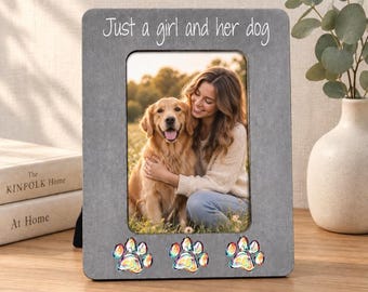 May include: A rectangular gray picture frame with the white text Just a girl and her dog printed at the top. The frame features three iridescent paw print embellishments along the bottom edge and contains a photograph of a golden retriever and a person.