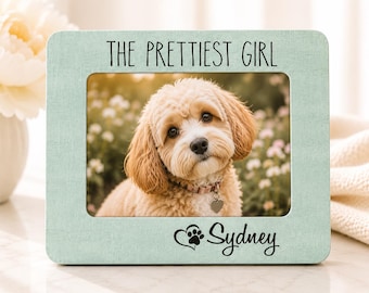 May include: A rectangular light green picture frame with a textured finish. The top border features the text THE PRETTIEST GIRL in black, and the bottom border displays a heart-shaped paw print icon followed by the name Sydney in black script.