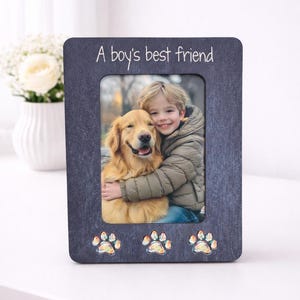 May include: A dark grey wooden picture frame with a wood-grain effect. The frame displays a photo of a boy and a golden retriever. The text "A boy's best friend" is at the top, with paw prints at the bottom.