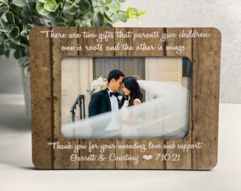 May include: A rustic wooden photo frame with a wedding photo of a couple. The frame has a quote about parents giving children roots and wings. The text below the photo reads "Thank you for your unending love and support. Garrett & Courtney 7.10.21".