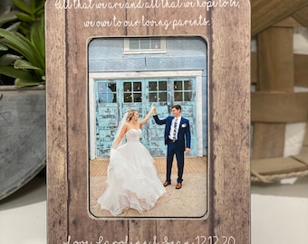 May include: A rustic wooden picture frame with a white inscription that reads "All that we are and all that we hope to be, we owe to our loving parents. Love, Caroline & Sean 12.12.20". The frame has a photo of a bride and groom in front of a blue door.