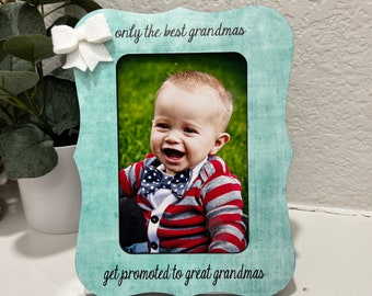 May include: A light blue picture frame with a white bow on the top left corner. The frame has the text "only the best grandmas get promoted to great grandmas" on it. A photo of a baby boy is in the frame.