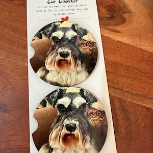May include: Two car coasters featuring a Schnauzer dog portrait. The coasters are round with a cutout for cup holders. A card above the coasters reads "Car Coaster" and a message about keeping cup holders clean.