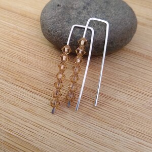 May include: A pair of silver earrings with a line of amber-colored crystals hanging from each.
