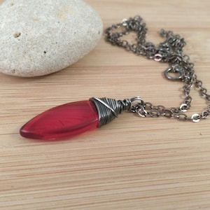 May include: A red glass pendant wrapped in silver wire hangs from a silver chain necklace.