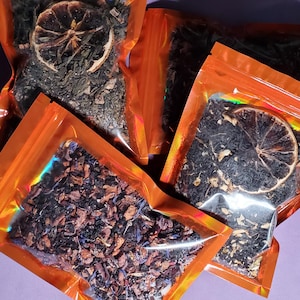 Può includere: Tre bustine arancioni di tè sfuso con frutta secca e fette di agrumi. Le miscele di tè sono visibili attraverso le bustine di plastica trasparenti.