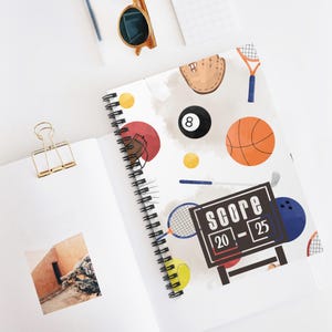 May include: A white spiral notebook with a colourful sports theme. The cover features a variety of sports equipment, including a basketball, baseball glove, tennis racket, golf club, and a pool ball. The text "SCORE 20 - 25" is printed on a black scoreboard.