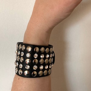 May include: A black leather bracelet with silver studs and clear rhinestones.