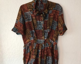 Könnte beinhalten: Ein Vintage-Kleid in einem braunen, blauen und grünen gemusterten Stoff mit Knopfleiste und kurzen Ärmeln.
