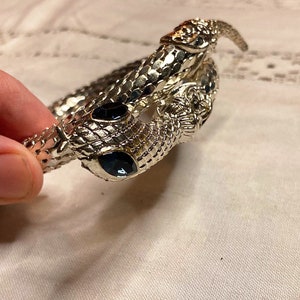 May include: Silver snake bracelet with black gem eyes. The snake is coiled and the tail is curled up.