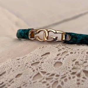 Könnte beinhalten: Ein grünes Lederarmband mit einem goldenen Doppel-'G'-Logo-Verschluss.