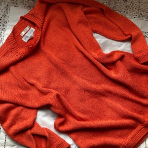 May include: A burnt orange knitted jumper with a crew neck and long sleeves.