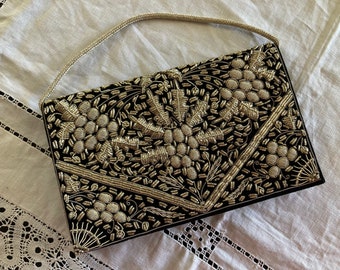 Può includere: Una borsa da sera in velluto nero con una tracolla a catena argentata. La borsa è ricamata con un motivo floreale in filo argentato.